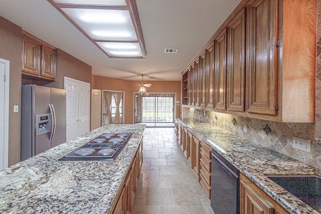 kitchen featuring stainless steel fridge, stone tile floors, brown cabinetry, dishwasher, and black electric stovetop