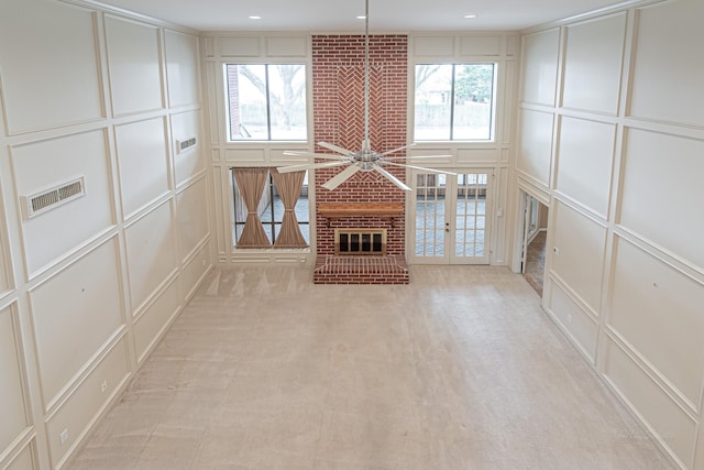 unfurnished living room with a brick fireplace, plenty of natural light, visible vents, and a decorative wall