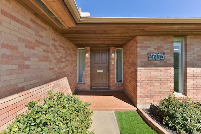 view of exterior entry featuring covered porch and brick siding