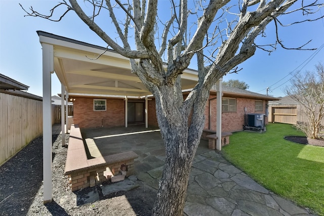 back of property featuring a fenced backyard, a yard, central air condition unit, a patio area, and brick siding