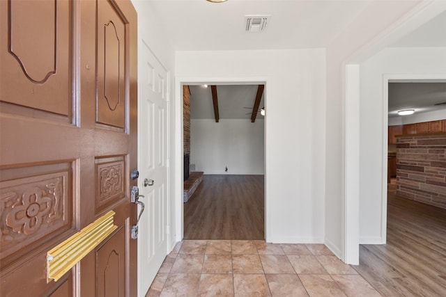 entryway featuring beam ceiling, visible vents, a fireplace, and light tile patterned flooring