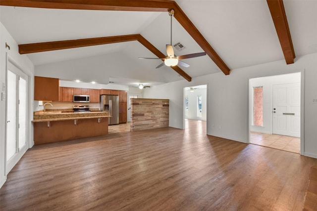 unfurnished living room featuring ceiling fan, a sink, visible vents, light wood-style floors, and beam ceiling