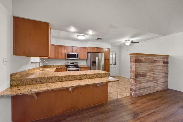 kitchen with light stone counters, brown cabinets, appliances with stainless steel finishes, a sink, and a peninsula