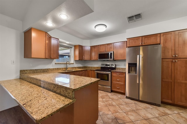 kitchen with visible vents, brown cabinetry, a peninsula, stainless steel appliances, and a sink