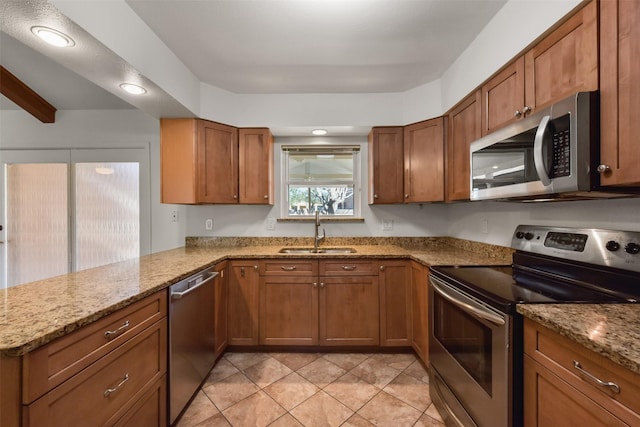 kitchen featuring light stone counters, brown cabinets, stainless steel appliances, a sink, and a peninsula