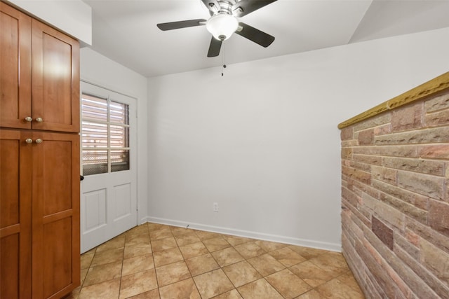 spare room with a ceiling fan, brick wall, baseboards, and light tile patterned floors