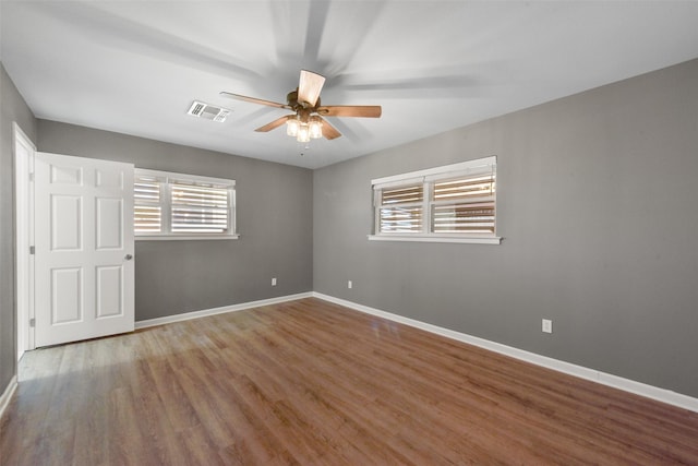 unfurnished room with a ceiling fan, wood finished floors, visible vents, and baseboards