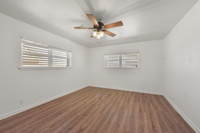 spare room featuring ceiling fan, plenty of natural light, wood finished floors, and baseboards