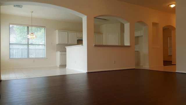 unfurnished living room featuring a notable chandelier, wood finished floors, visible vents, and baseboards