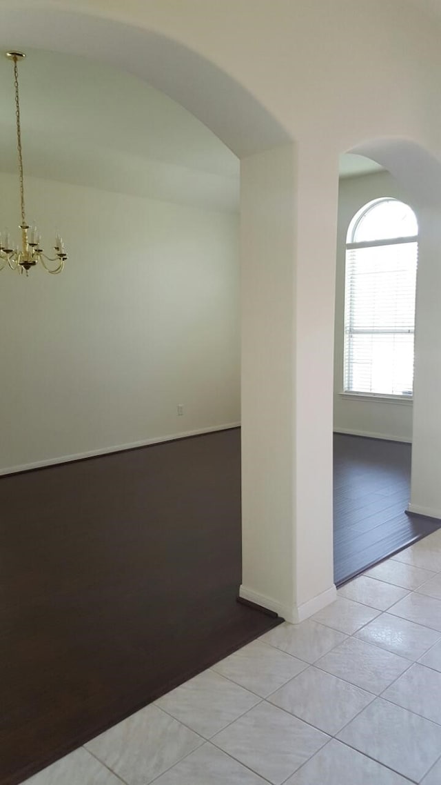 unfurnished room with arched walkways, light tile patterned flooring, baseboards, and an inviting chandelier