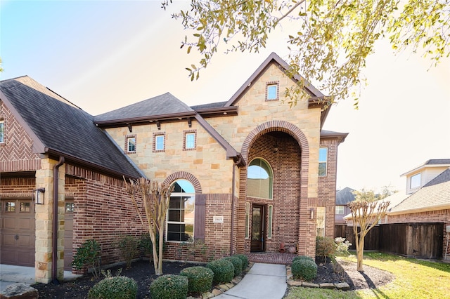 view of front of home featuring brick siding, a shingled roof, fence, a garage, and stone siding