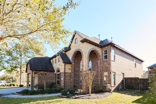 view of side of home with stone siding, brick siding, a lawn, and fence