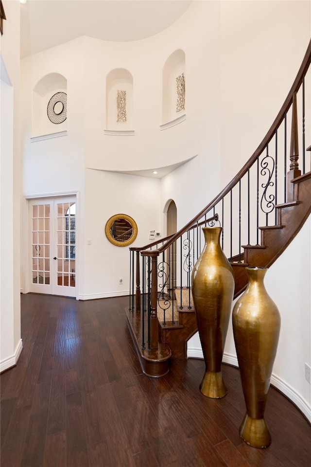 stairway featuring hardwood / wood-style floors, french doors, baseboards, and a towering ceiling