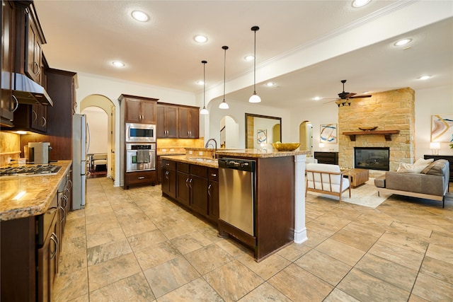 kitchen featuring arched walkways, ceiling fan, a stone fireplace, stainless steel appliances, and backsplash