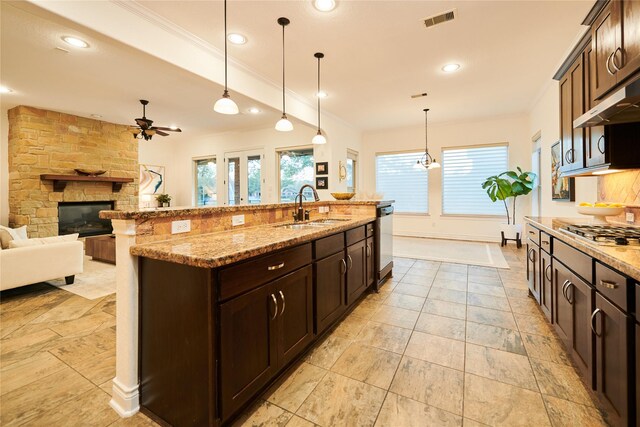 kitchen featuring visible vents, a sink, appliances with stainless steel finishes, a stone fireplace, and crown molding