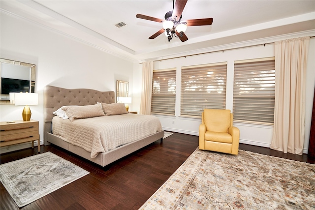 bedroom with visible vents, ornamental molding, a ceiling fan, a tray ceiling, and dark wood-style flooring