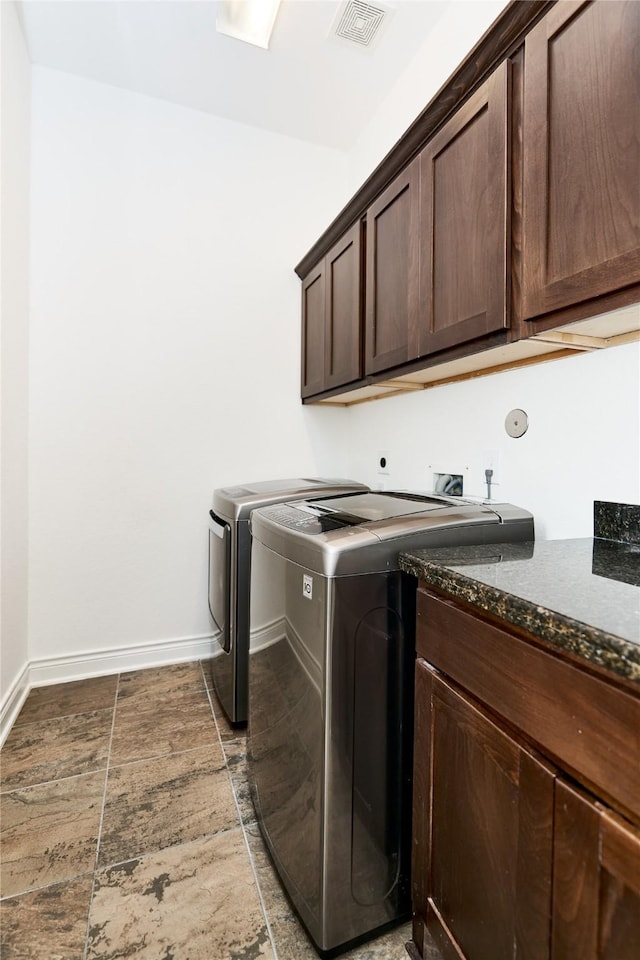 clothes washing area with visible vents, baseboards, washer and dryer, cabinet space, and stone finish floor