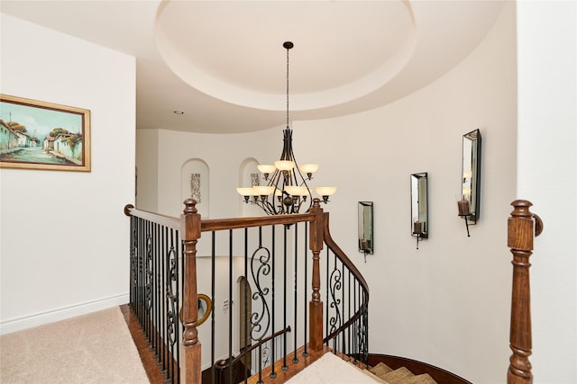 staircase with a tray ceiling, baseboards, a chandelier, and carpet flooring