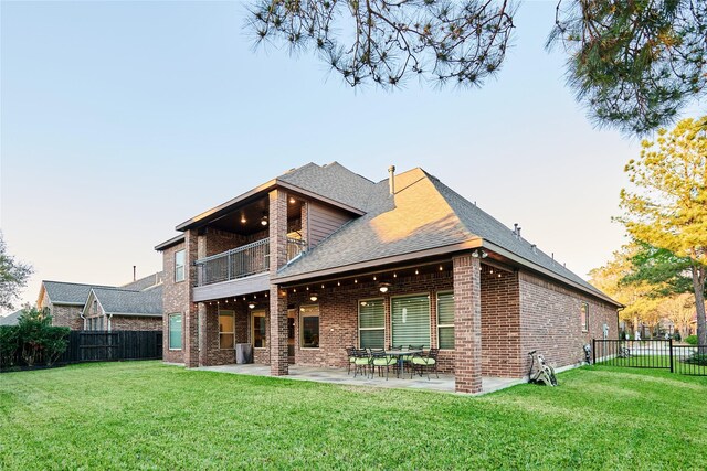 rear view of house with a patio, a balcony, a yard, a fenced backyard, and brick siding