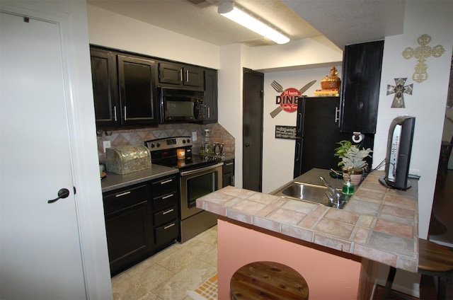 kitchen with a breakfast bar, backsplash, a sink, a peninsula, and black appliances