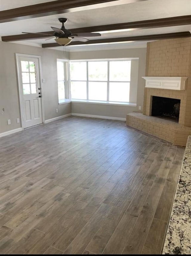 unfurnished living room featuring dark wood-style floors, baseboards, a fireplace, and beamed ceiling