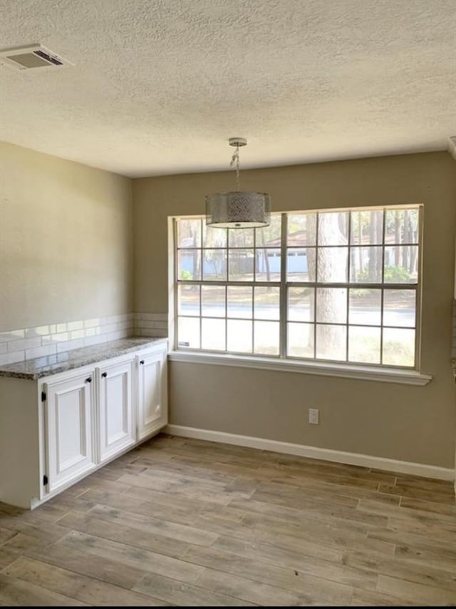 unfurnished dining area featuring a textured ceiling, light wood-type flooring, visible vents, and baseboards