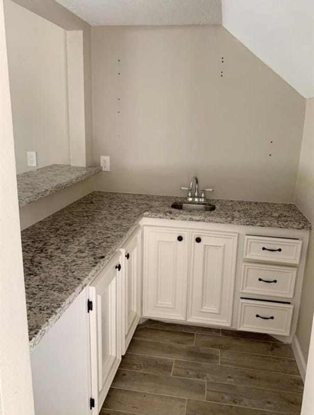 interior space featuring light stone countertops, wood tiled floor, vaulted ceiling, and a sink