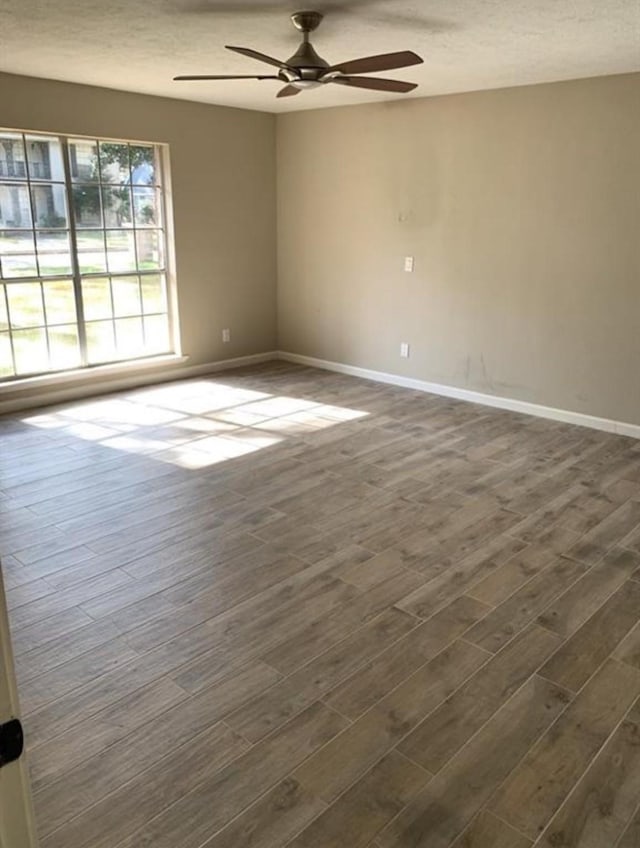 empty room featuring a textured ceiling, dark wood-type flooring, a ceiling fan, and baseboards