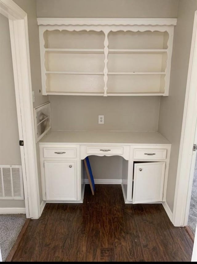 unfurnished office with dark wood-type flooring, built in study area, visible vents, and baseboards