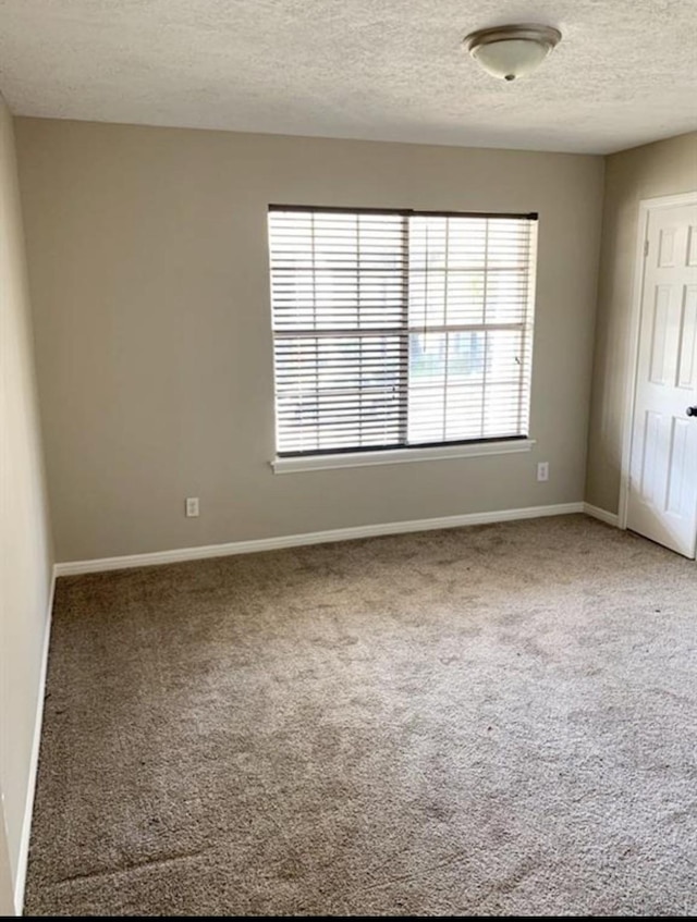 carpeted empty room featuring a textured ceiling and baseboards