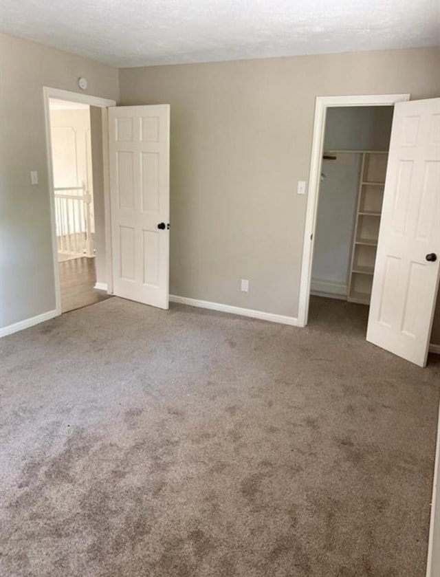 unfurnished bedroom with a textured ceiling, carpet flooring, baseboards, a spacious closet, and a closet