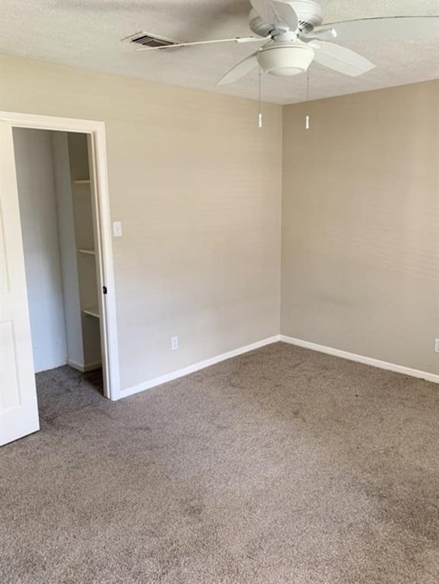 spare room with a textured ceiling, carpet floors, ceiling fan, and visible vents