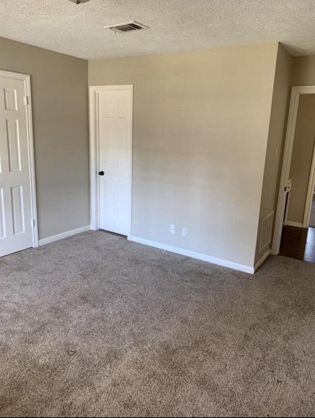 carpeted empty room featuring visible vents, a textured ceiling, and baseboards