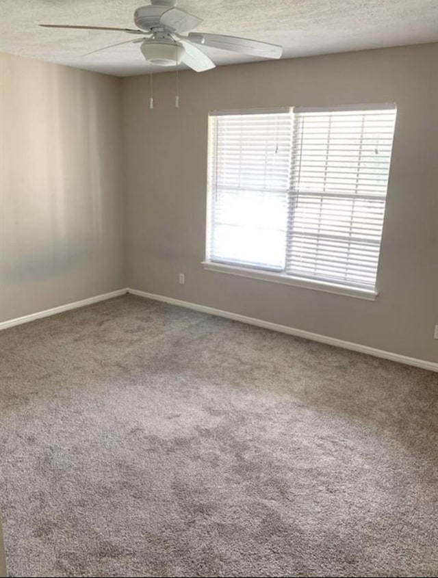 spare room with a textured ceiling, carpet, a ceiling fan, and baseboards