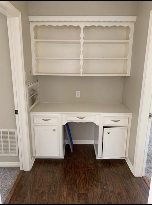 unfurnished office with baseboards, visible vents, dark wood-type flooring, and built in desk