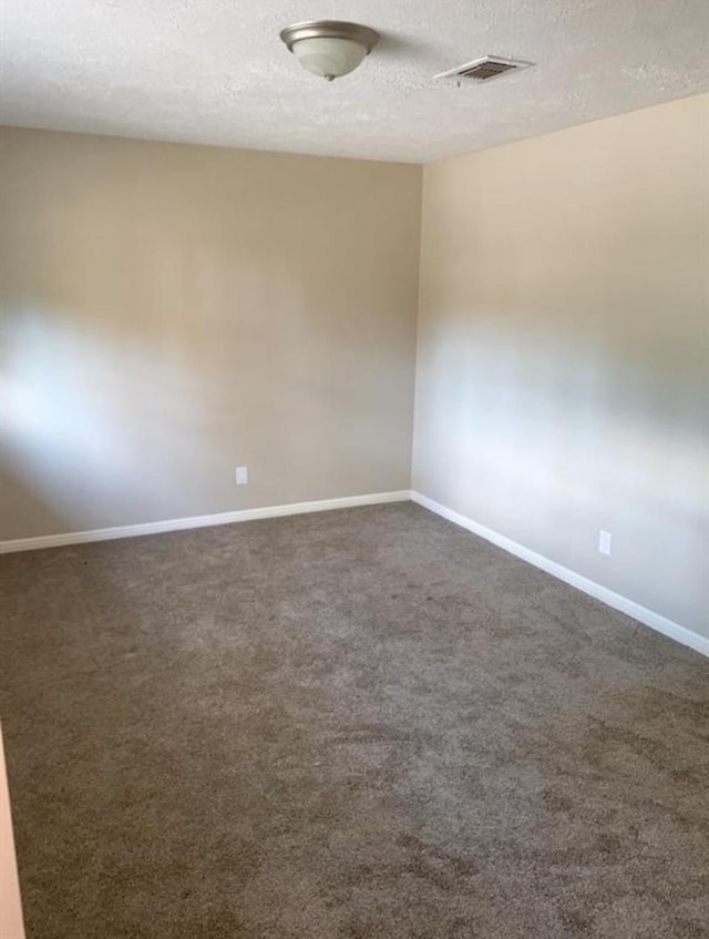 empty room featuring a textured ceiling, dark carpet, visible vents, and baseboards