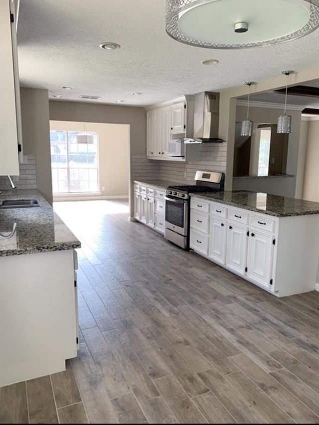 kitchen featuring stainless steel gas stove, a sink, wall chimney range hood, and wood finished floors