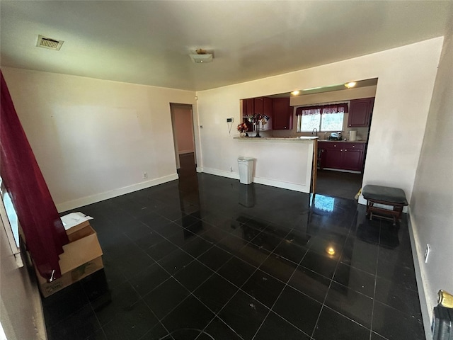 kitchen with visible vents, dark brown cabinets, a peninsula, dark tile patterned floors, and baseboards