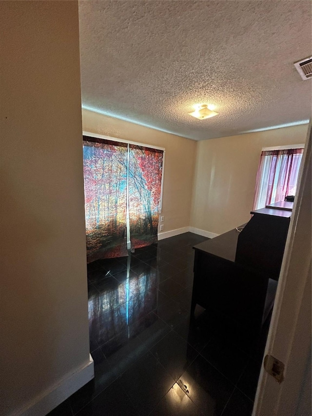 spare room featuring a textured ceiling, dark tile patterned floors, visible vents, and baseboards