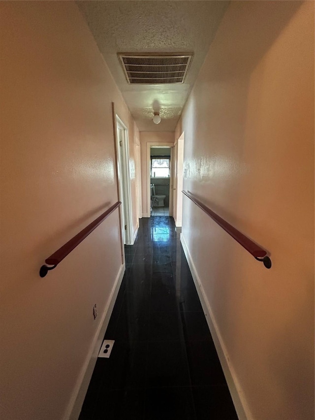 corridor featuring visible vents, dark tile patterned floors, and baseboards