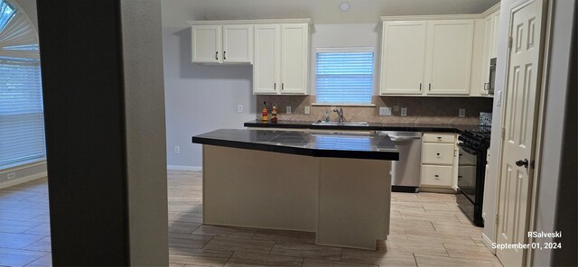 kitchen with black gas range, dark countertops, backsplash, stainless steel dishwasher, and a sink