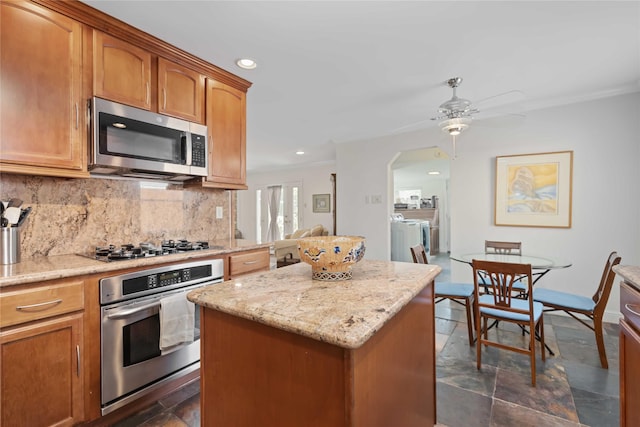 kitchen featuring arched walkways, stainless steel appliances, a kitchen island, independent washer and dryer, and decorative backsplash