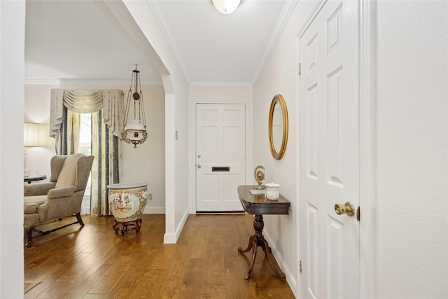 foyer entrance featuring baseboards, arched walkways, crown molding, and wood finished floors