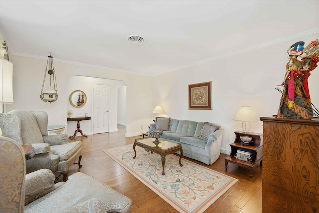 living area with arched walkways, visible vents, light wood-style floors, ornamental molding, and baseboards