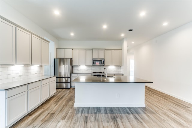 kitchen featuring decorative backsplash, an island with sink, light wood-style flooring, appliances with stainless steel finishes, and a sink