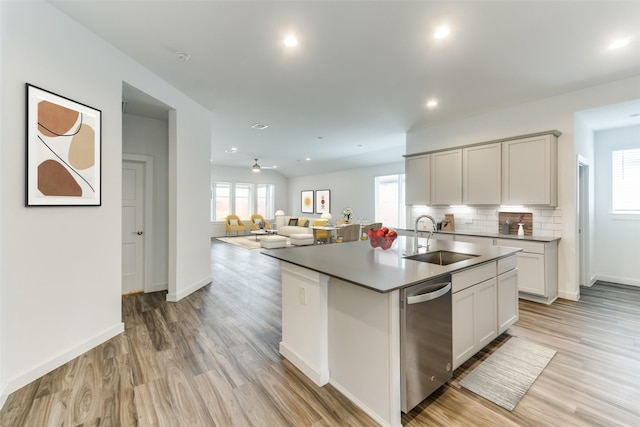 kitchen featuring decorative backsplash, a sink, a kitchen island with sink, light wood-type flooring, and stainless steel dishwasher