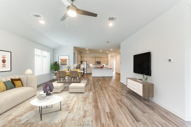 living room featuring visible vents, vaulted ceiling, light wood-style flooring, and baseboards