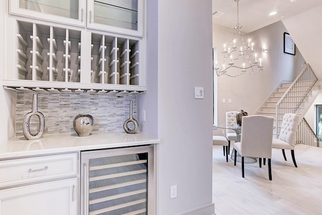 bar with tasteful backsplash, visible vents, light wood-style floors, beverage cooler, and stairs