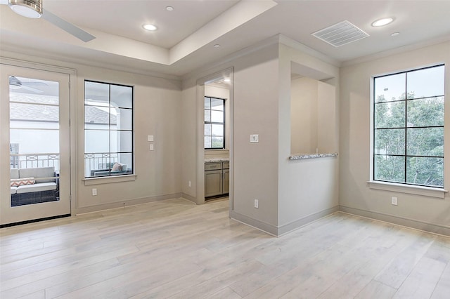 empty room with a tray ceiling, light wood-style flooring, visible vents, and baseboards