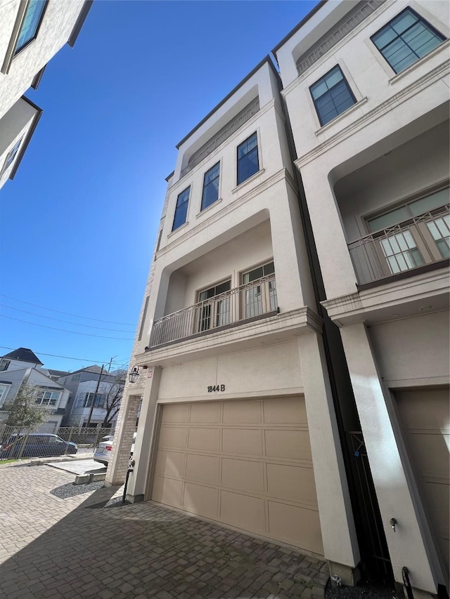 exterior space featuring a garage, fence, decorative driveway, and stucco siding